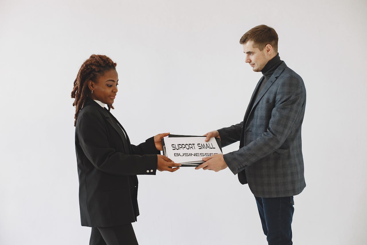 Two business professionals exchanging a box labeled 'Support Small Businesses' in a studio setting.