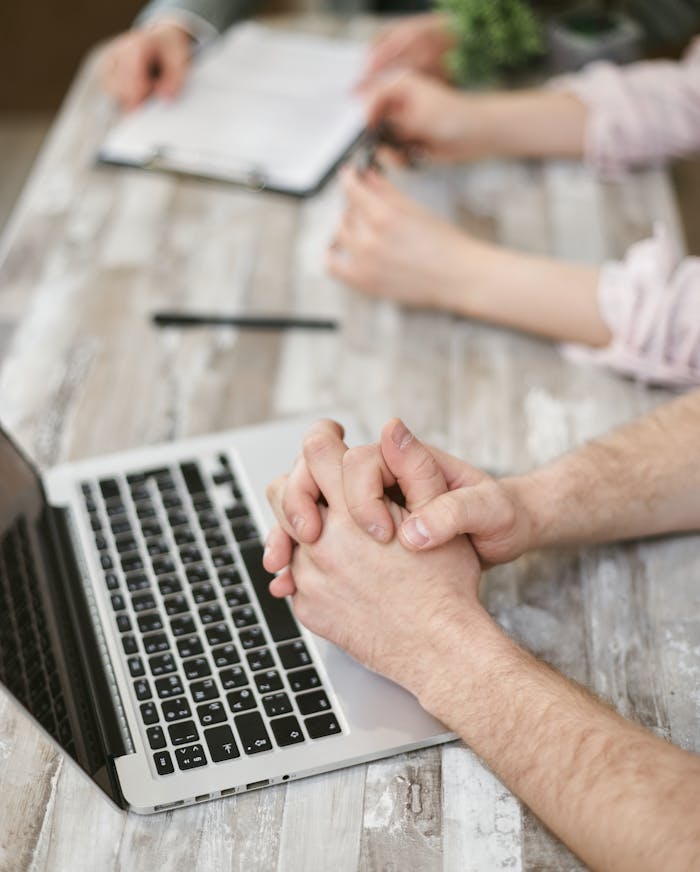 Close-up of hands during a business meeting with a laptop and documents on a wooden table.